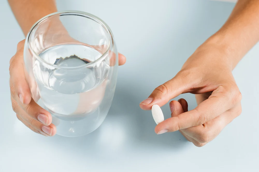 hands holding a white supplement tablet and a glass of water